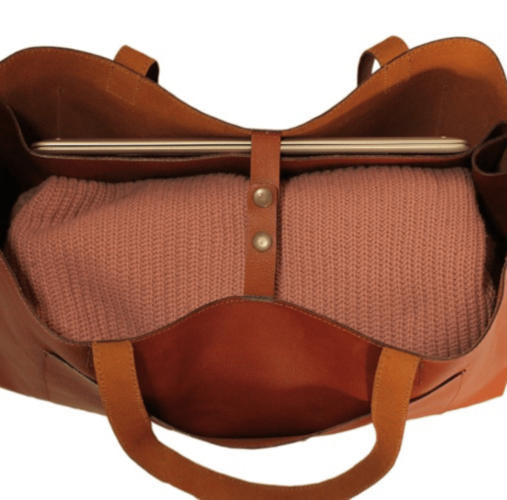 A tan leather bag featuring a pink blanket within, representing a chic and inviting accessory.