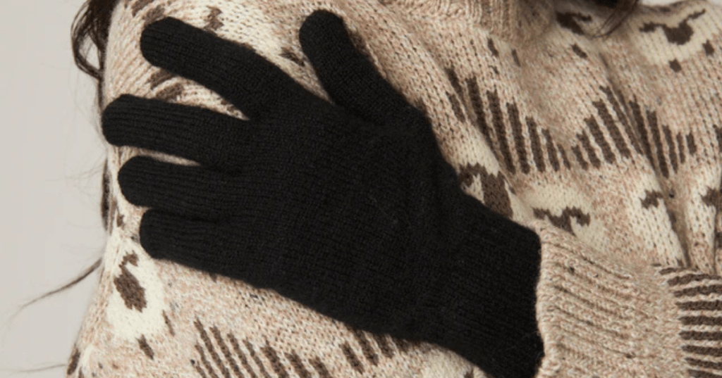 Pair of black lambs wool gloves being modelled by a woman wearing a knitted sheep jumper.