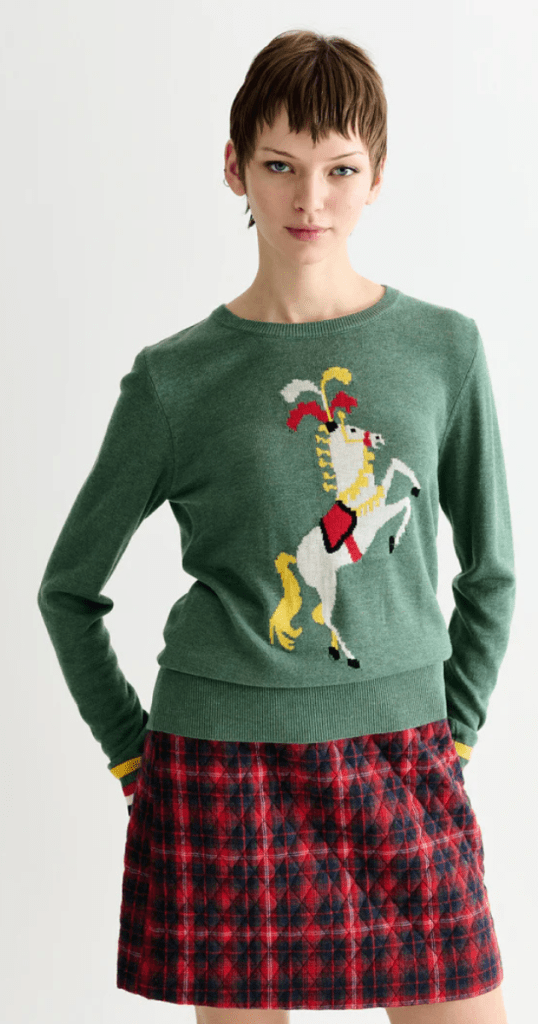 A woman dressed in a green sweater adorned with a circus horse and plaid skirt.