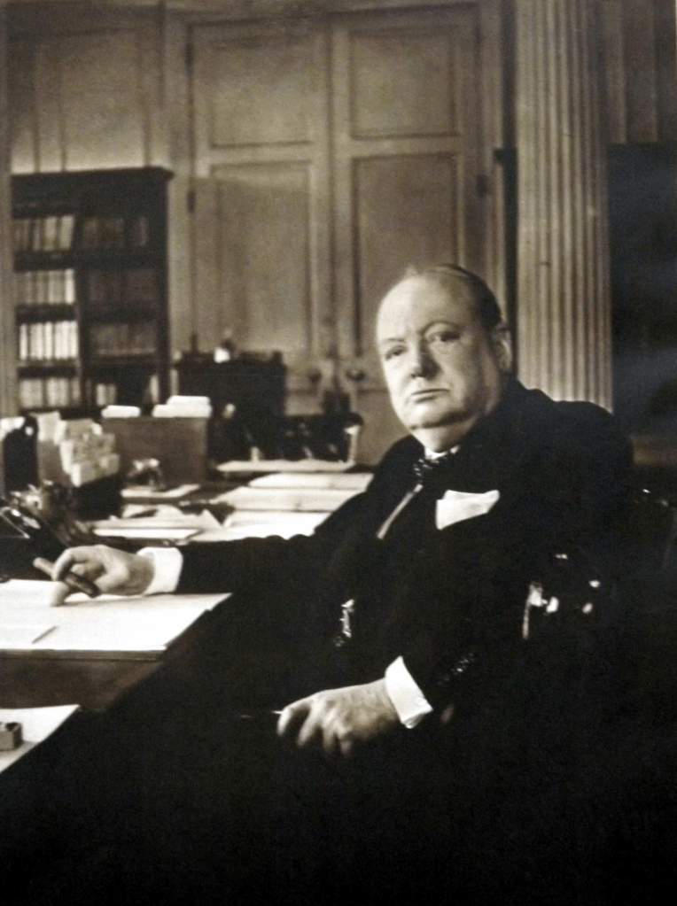 Image of Winston Churchill looking directly at the camera while seated at his desk.