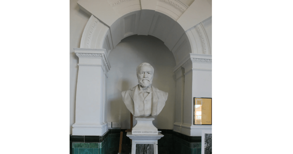 White marble bust of a Andrew Carnegie displayed in an arched alcove, set against a simple interior background.