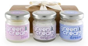 Three jars of “green cream” skincare—variants “love,” “original,” and “dream”—with pastel pink, purple, and blue labels, sealed with metallic lids. Displayed in front of a wooden gift box tied with a cream ribbon, a bundled set. Branding features a playful figure and whimsical typography, ideal for wellness or self-care gifting.