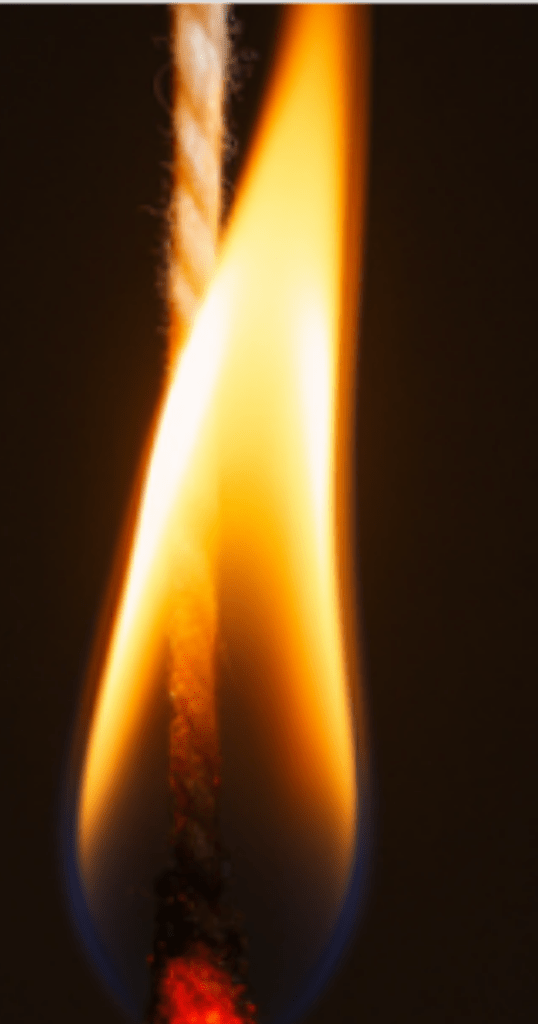 Close-up of a tampon string burning against a dark background. The flame glows with a bright yellow-orange hue and a small blue base. The wick is partially charred and glowing red, highlighting the combustion process.