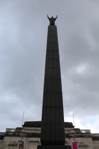Leverhulme Memorial outside the Lady Lever Gallery, featuring a tall obelisk topped with a winged figure. Set against a cloudy sky, the monument stands near the gallery’s classical façade with columns and ornate detailing, evoking a sense of civic pride and remembrance.
