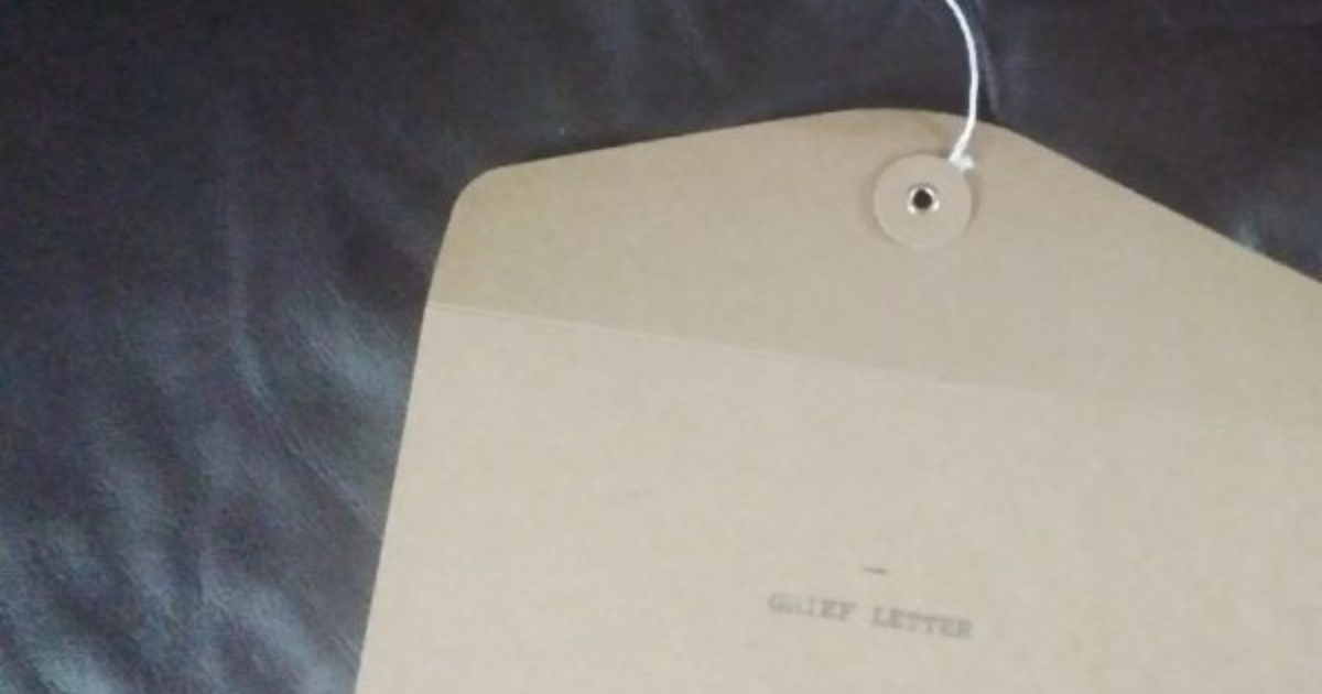 Brown string‑tie envelope lying on a dark surface. The envelope is made of thick kraft paper with a circular button-and-string closure at the top. A white rectangular label on the front reads “RELIEF LETTER” in bold capital letters. The envelope appears unopened and neatly positioned, suggesting it contains an important or official document.