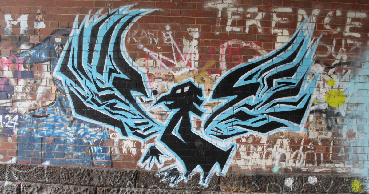 A Blue Liver Bird graffiti mural painted on a brick wall along the Liverpool Loop Line, with bold black and blue wing patterns standing out against layers of older street art in the background.