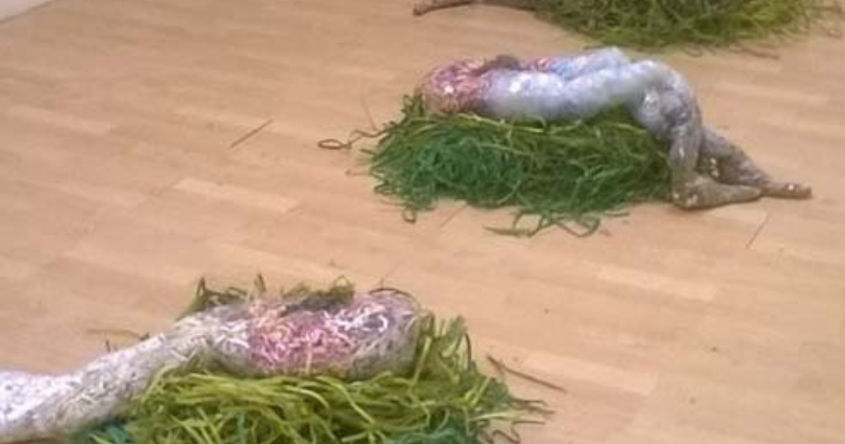 Installation view of sculptural forms from SV: Sex by Violence, exhibited at Zauhouse Gallery in Liverpool, showing three human‑shaped figures made from shredded materials and translucent wrapping arranged on green textured bases.