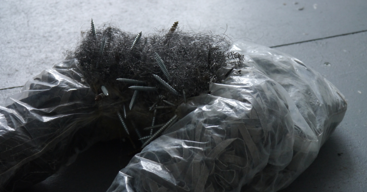 Invasion, part of the SV: Sex by Violence animated sculpture series, shown as a transparent plastic form packed with dark shredded material, with steel wool and protruding screws extending from one end on a grey gallery floor.