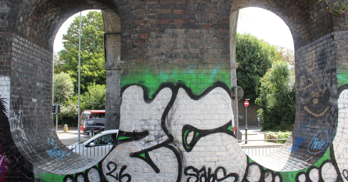 Graffiti-covered skate ramp beneath the High Wycombe Viaduct Skate Park, featuring a large white and black throw-up style piece painted on a curved brick structure framed by the viaduct's stone arches.